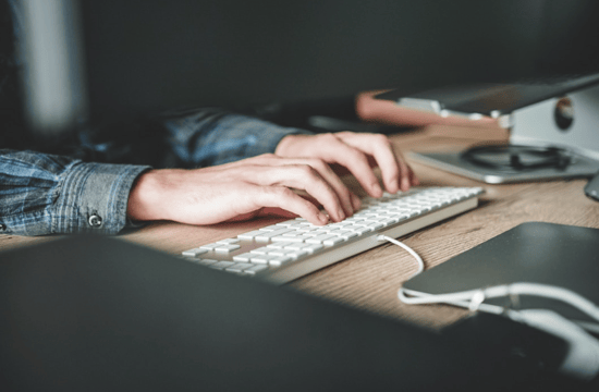 Individual typing on a keyboard at a desk, highlighting automation and scheduling tools for improved communication efficiency.