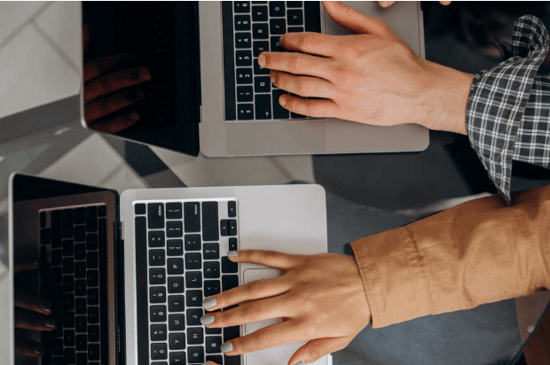 two professionals working on laptops at a shared table, representing digital collaboration and connected international business.