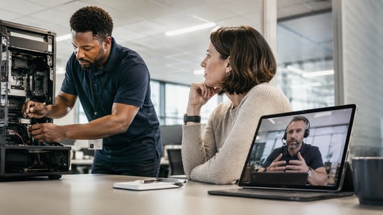 On-site IT technician repairing business equipment while an operations manager consults a remote support specialist by video call