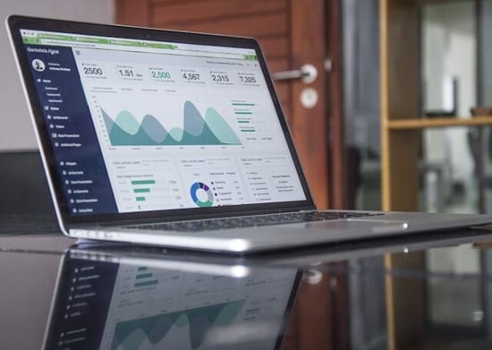 Laptop displaying a business analytics dashboard on a reflective conference table in an office setting.
