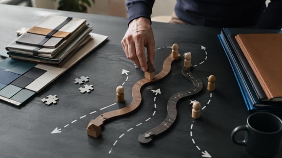 Hand arranging wooden pathway pieces and figures on a tabletop, representing different business choices, decision paths, and the ability to adapt when circumstances change.