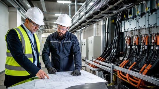Engineers reviewing electrical plans beside industrial power cables and control panels during a facility cable replacement project.