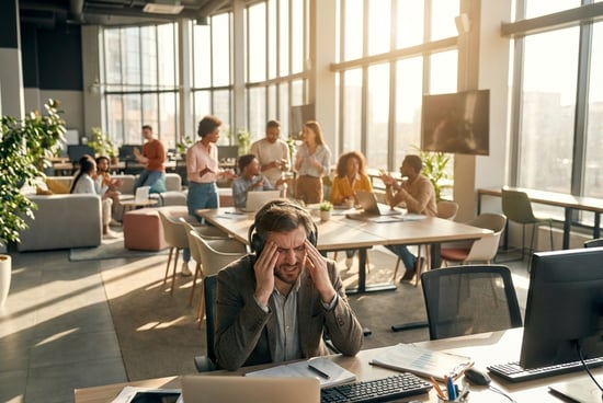 Man with a headache in a busy office environment.